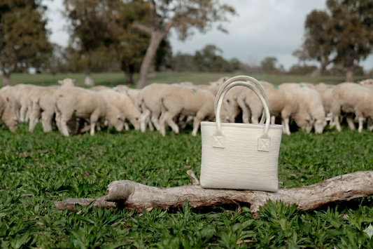 Australian wool tote bag in natural wool with matching handles and cotton lining, designed for professionals wanting to use a natural fibres.  Bag is in a beautiful paddock with sheep in the background representing the wool use in the bag. 