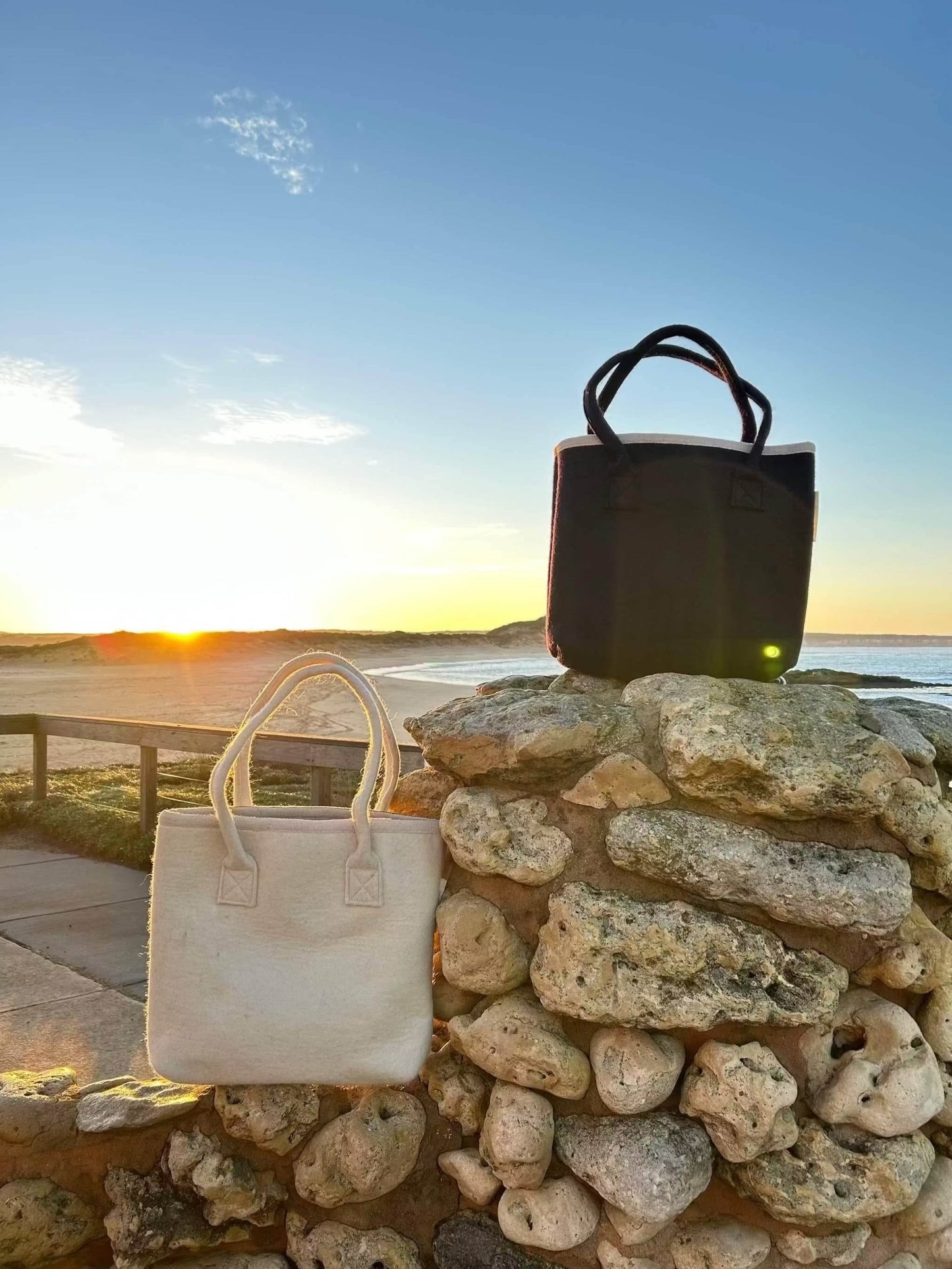 Australian wool tote bag in navy and natural wool colour with matching handles and cotton lining, designed for professionals wanting to use a natural fibres and sustainability.  Bags are on a stone wall in front of a beach, on sunrise. 