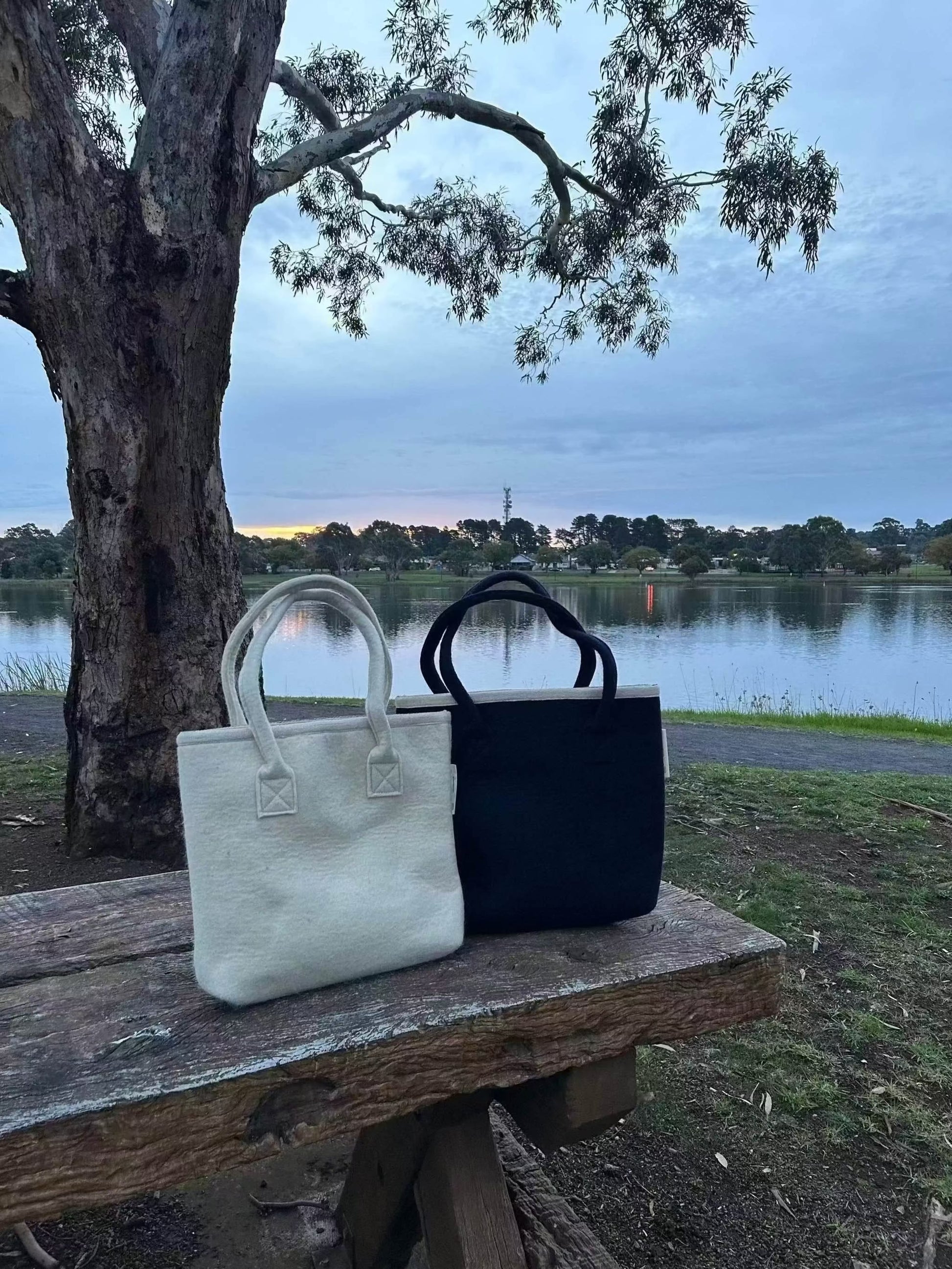 Australian wool tote bag in natural wool and navy with matching handles and cotton lining, designed for professionals wanting to use a natural fibres.  Bags are situated on a park bench with a lake in the background on sunset.  