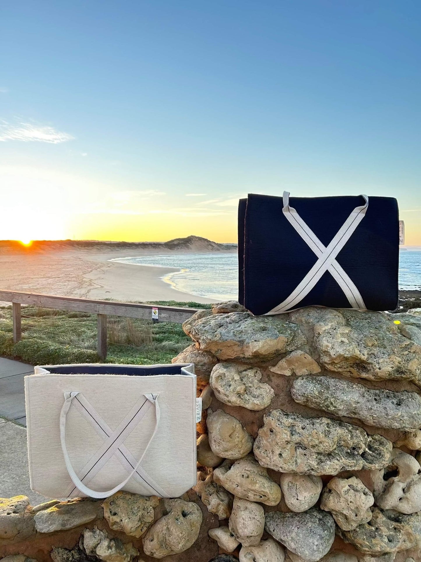 Everyday wool bag in natural wool and navy colour with cotton handles and cotton lining, showcasing versatile design for daily use and travel. Bags are on a stone wall in front of a beach, on sunrise. 