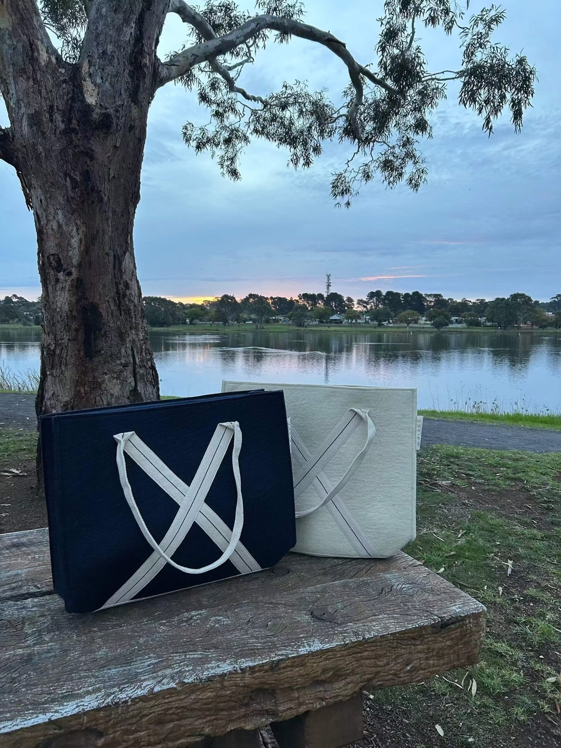 Everyday wool bag in natural wool and navy colour with cotton handles and cotton lining, showcasing versatile design for daily use and travel.  Bags are situated on a park bench with a lake in the background on sunset.  